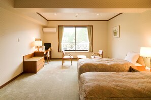 A hotel room with two beds, a desk with a chair, a small table, and a window with a view of trees. - Hotel Windsor (Nakatsugawa)
