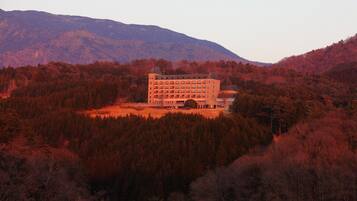A large, multi-story building surrounded by dense forest and mountains.