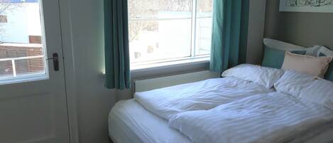A bedroom with a bed, a window with curtains, a radiator, and a door.