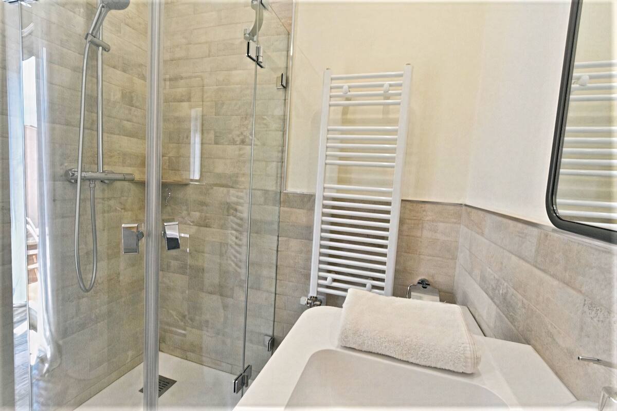 A modern bathroom with a glass-enclosed shower, a white bathtub, and a towel rack.