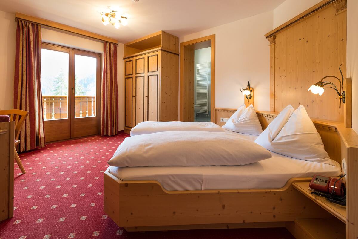 Habitación de hotel con cama de madera, un escritorio y un balcón con cortinas.