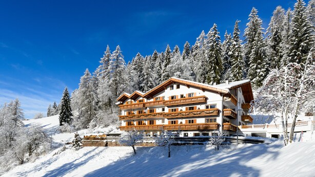 Ein mehrstöckiges Hotel mit Balkonen, umgeben von schneebedeckten Bäumen und blauem Himmel.