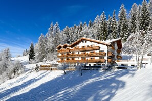 Un hotel de varios pisos con balcones, rodeado de árboles cubiertos de nieve y un cielo azul despejado.