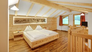 Ein Schlafzimmer aus Holz mit schrägen Wänden, einem Bett, einem Nachttisch, einem Schreibtisch und einem Fenster mit Vorhängen.