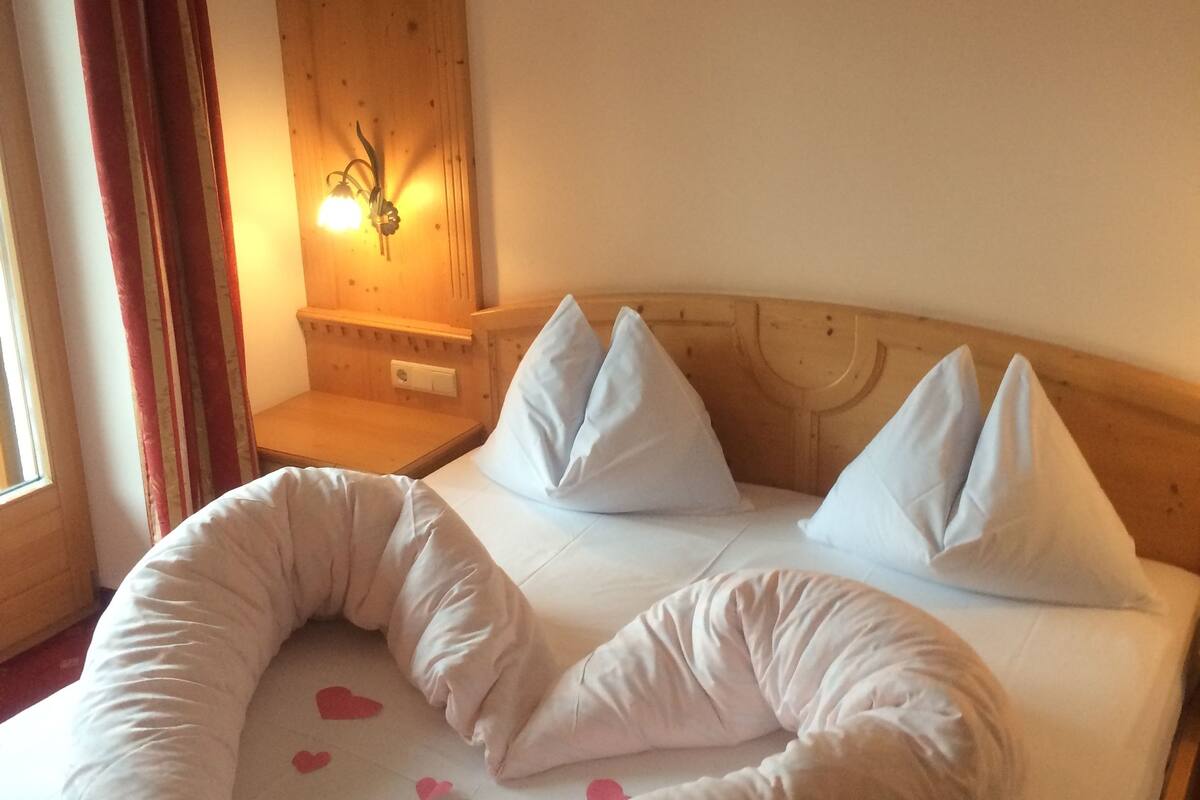 Una cama con una disposición de almohadas en forma de corazón y una lámpara fijada a la pared.