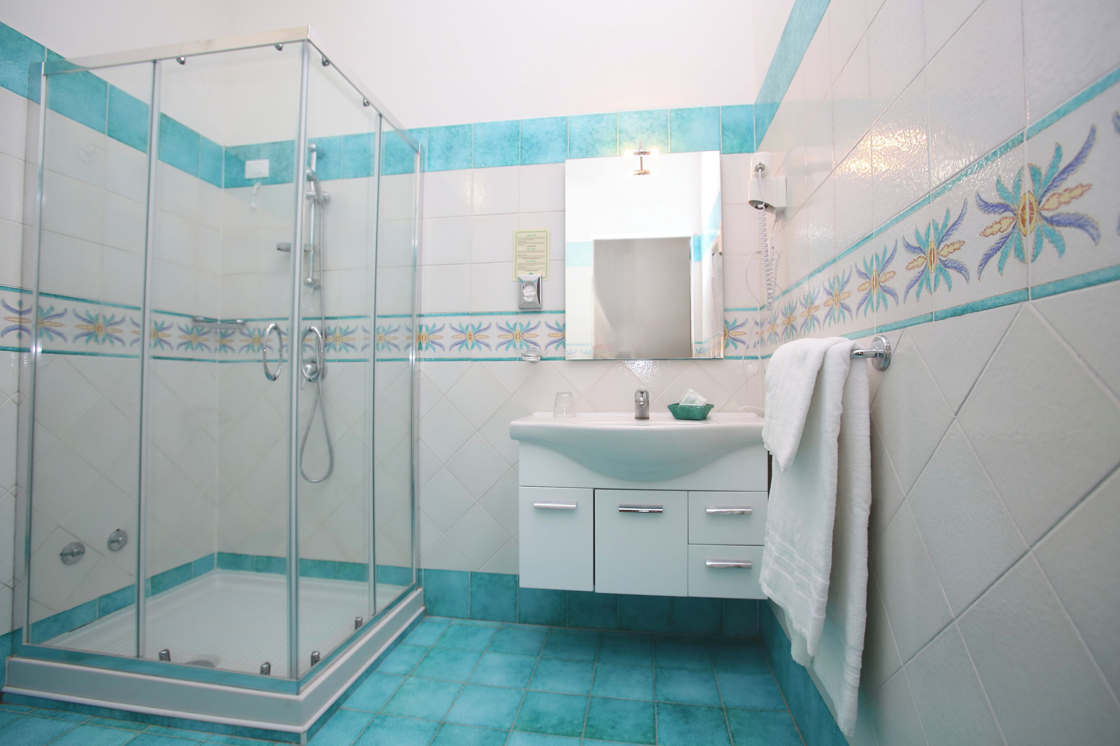 Casa de banho com cabine de duche em vidro, lavatório com espelho e chão em mosaico.