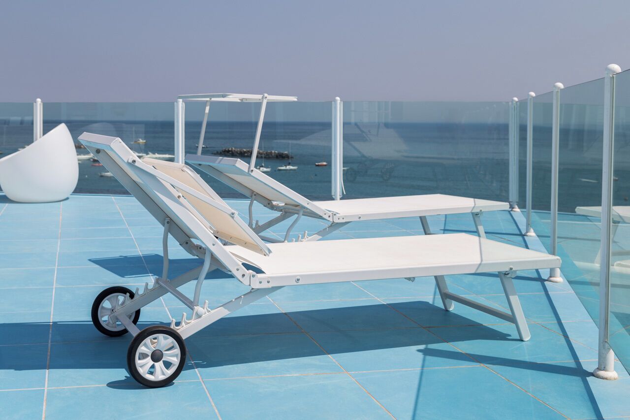 Una tumbona con ruedas sobre una terraza de azulejos azules junto al mar.