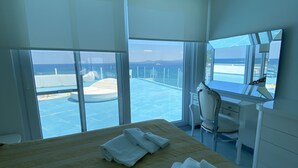 A hotel room with a bed, a desk, and a large window offering a view of the sea and wind turbines. - Hotel Solemare Beach & Beauty SPA (Ischia)