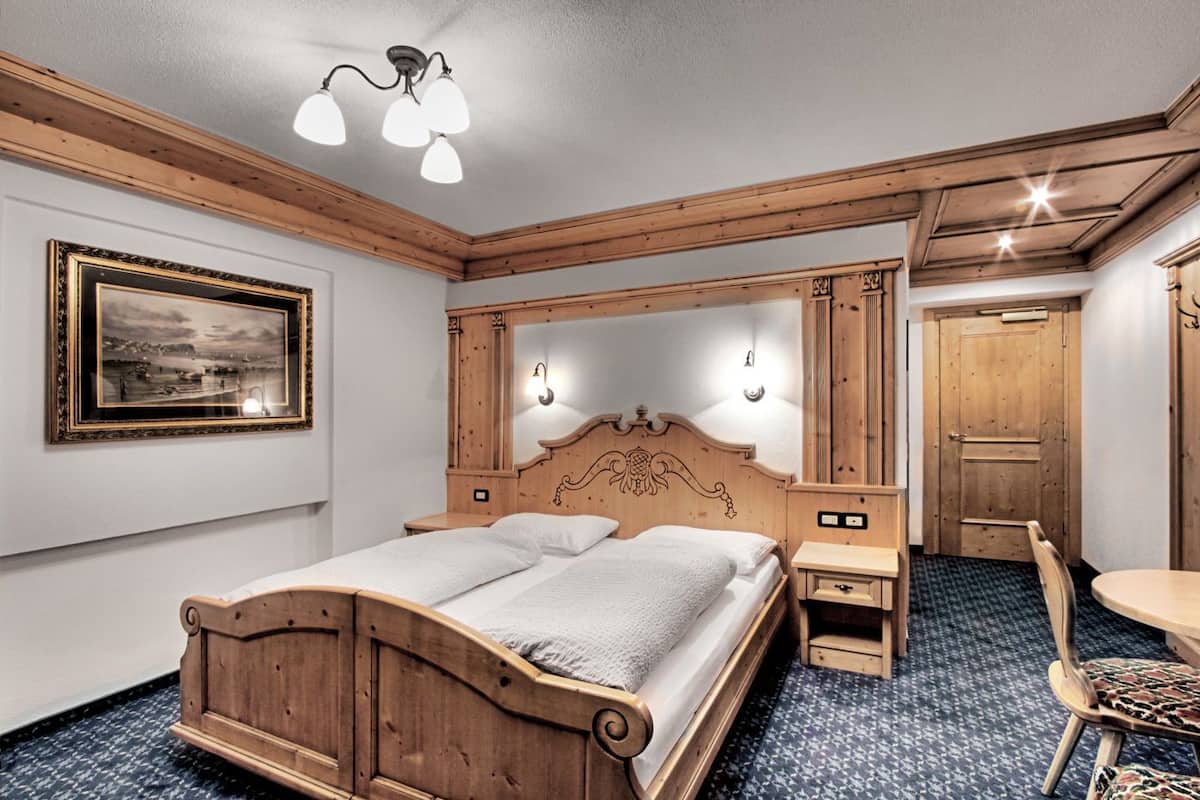 A wooden bedroom with a bed, bedside tables, a mirror, and a chair.