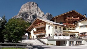 Un hotel de varios pisos con balcones decorados con flores, un letrero para bar-café y un paisaje de montaña al fondo.