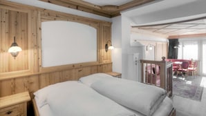 Un dormitorio con paneles de madera, una cama con ropa de cama blanca, una mesita de noche y vistas a un comedor con sillas rojas.