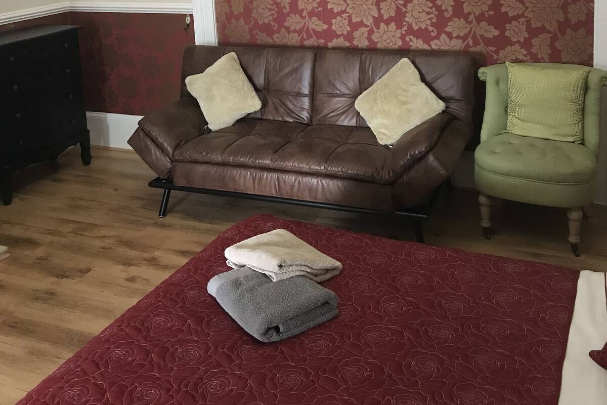 Una sala de estar con un sofá de cuero marrón, un sillón verde y una pared con estampado floral rojo.