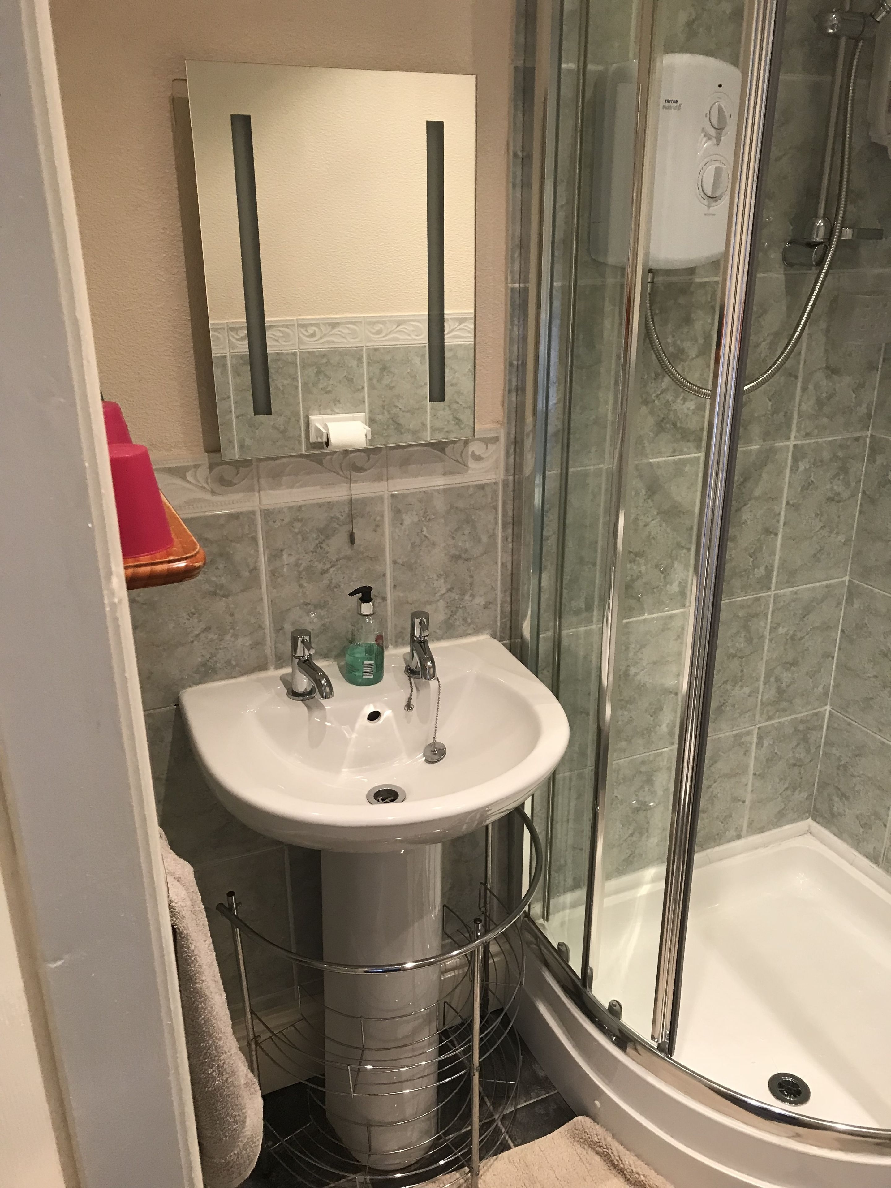 Une salle de bain avec un lavabo blanc, une cabine de douche en verre et un porte-rouleau de papier toilette fixé au mur.