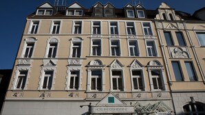Un immeuble à plusieurs étages de style architectural classique, caractérisé par des encadrements de fenêtres ouvragés et des éléments décoratifs. L’immeuble porte une enseigne indiquant « Hôtel Rheydter Residenz » et une autre indiquant « Weinkirch ».
