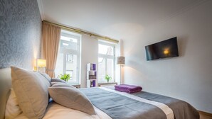 Une chambre d’hôtel avec un lit, un téléviseur fixé au mur et une fenêtre avec des rideaux.