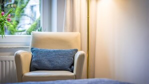 Une chaise avec un coussin à texture particulière, dans une pièce dotée d’une fenêtre, de rideaux et d’un radiateur.