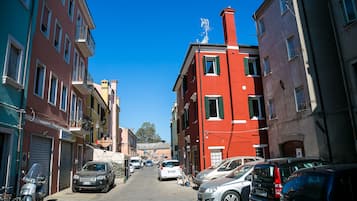 Eine schmale Straße gesäumt von bunten Häusern, parkenden Autos und wolkenlosem, blauem Himmel.