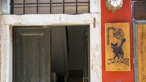 An open wooden door leading into a room with a red wall and a wooden sign with a cat and a cane. - Casa Sansera B&B (Chioggia)