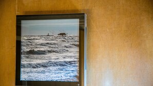 A framed photograph of a coastal scene with waves and a lighthouse. - Casa Sansera B&B (Chioggia)