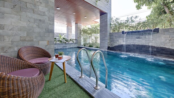 A swimming pool area with a stone wall, two wicker chairs, a small table, and a metal pool ladder. - Animor Green Home Da Nang (Da Nang)