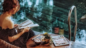 A person reading a book at a table with a coffee cup, a plant, and a magazine. - Animor Green Home Da Nang (Da Nang)