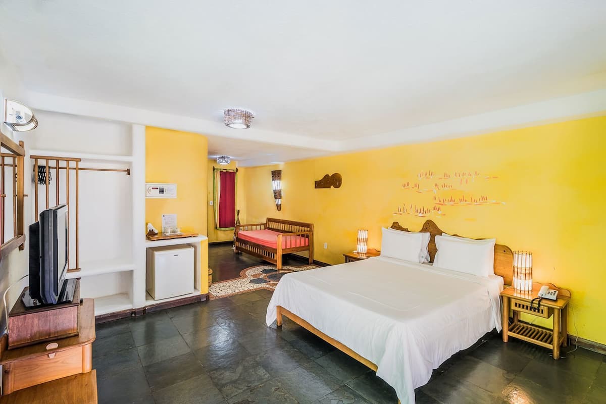 Camera d'albergo con un letto, comodini, una scrivania, una TV, una tenda rossa e una parete gialla.