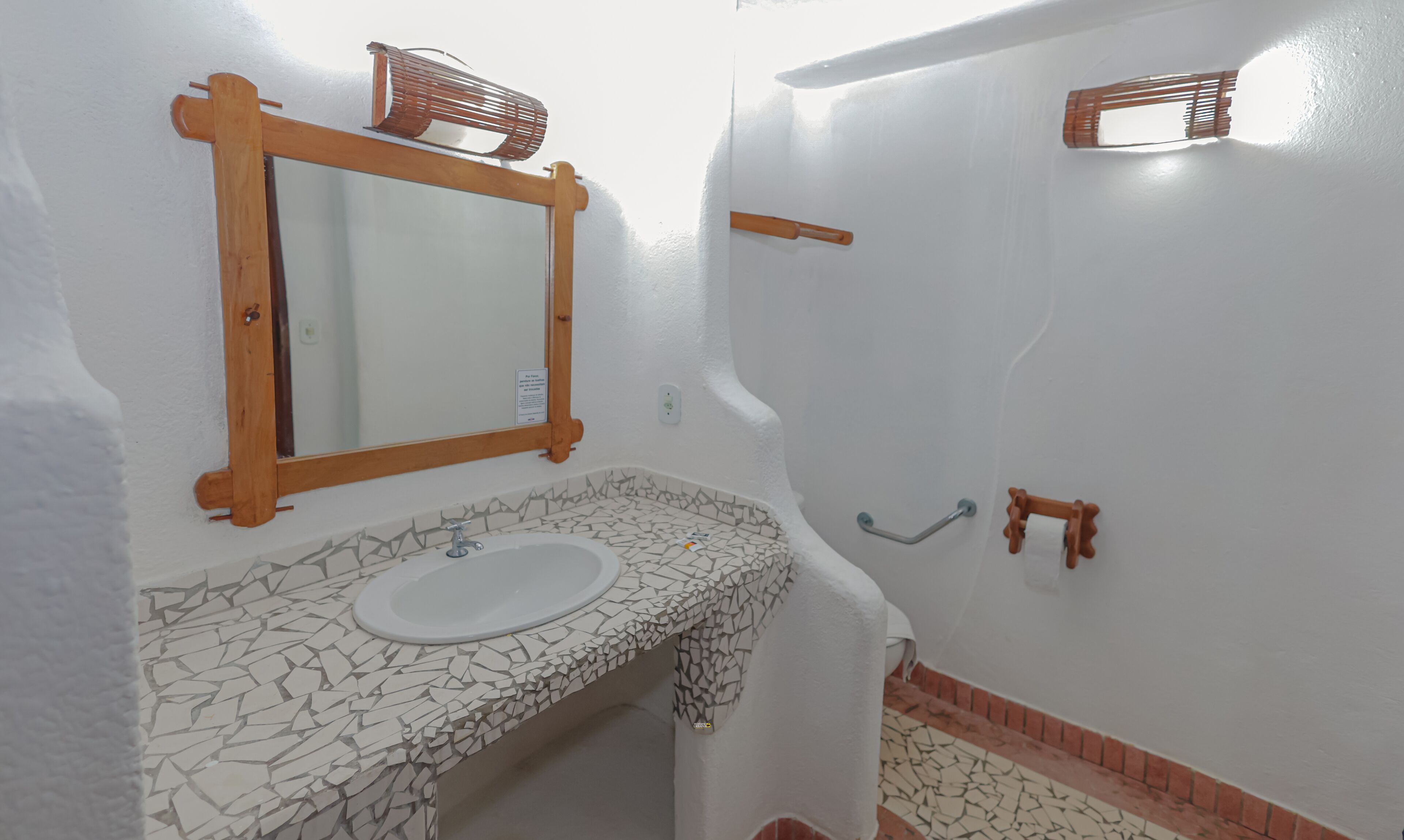 Un baño con lavamanos blanco, espejo con marco de madera, encimera con diseño de mosaico y zona de ducha.