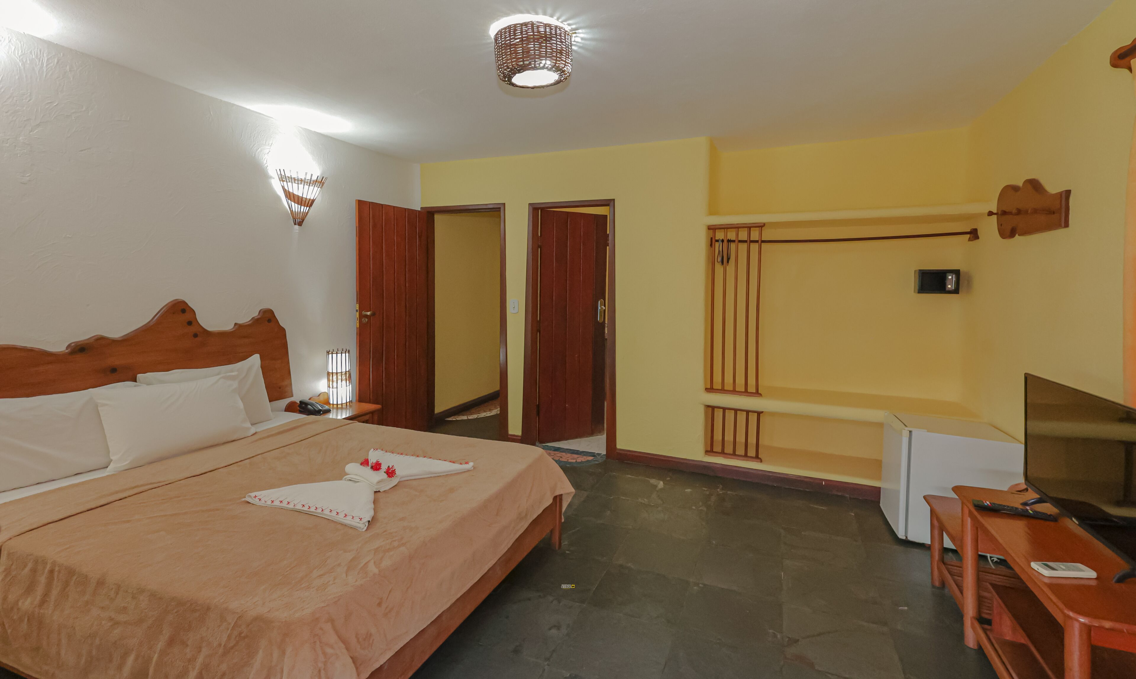 A hotel room with a bed, bedside table, lamp, wardrobe, and a television.