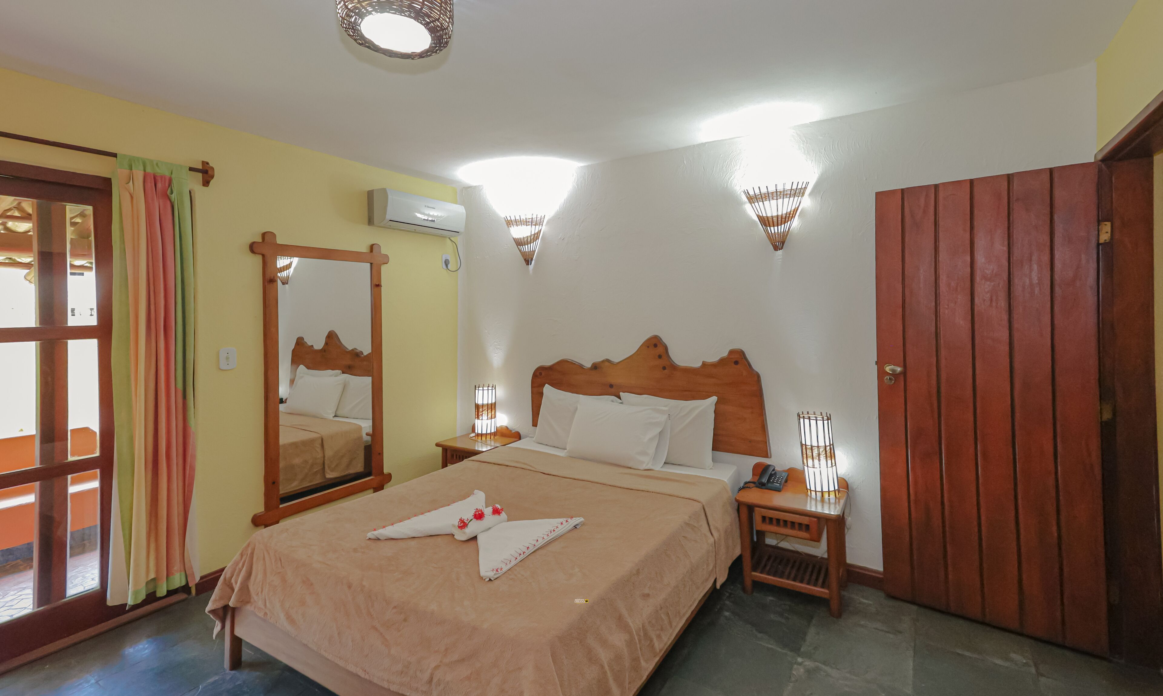 Een hotelkamer met een bed, nachtkastjes, een garderobe, een airconditioner en een raam met gordijnen.
