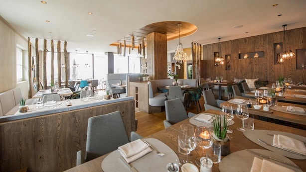 Een modern restaurant met houten details, ronde tafels en sfeerverlichting.