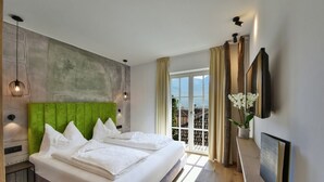 Een moderne hotelkamer met een groot bed, een groen gestoffeerd hoofdeinde, een groot raam met uitzicht en een flatscreen televisie aan de muur.