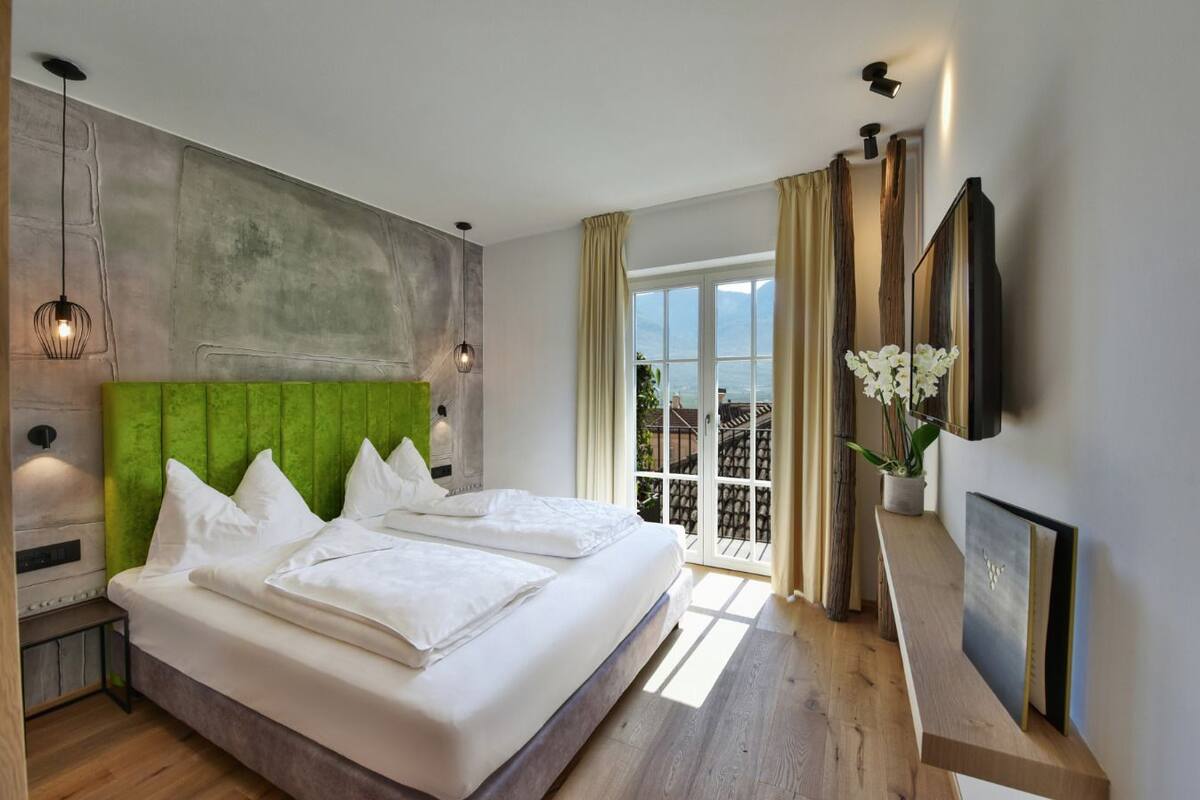 Een moderne hotelkamer met een groot bed, een groen gestoffeerd hoofdeinde, een groot raam met uitzicht en een flatscreen televisie aan de muur.
