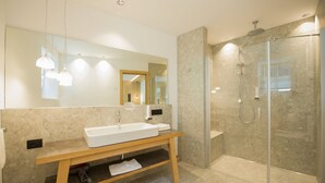 Een moderne badkamer met een grote spiegel, een houten wastafelmeubel, een witte wasbak en een douche met glazen wanden.