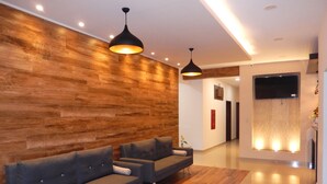 A modern lobby with wooden paneling, two grey sofas, and pendant lighting.