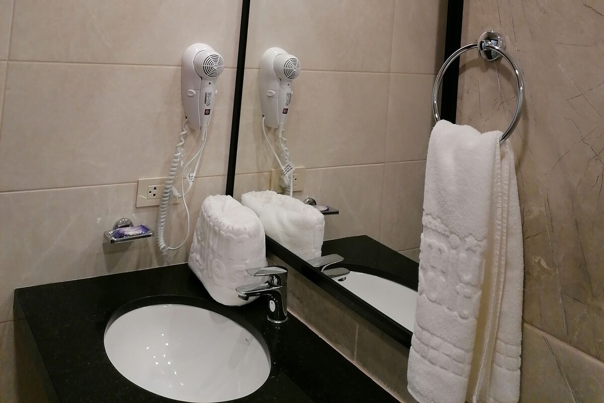 A bathroom with a large mirror, a black sink, two hair dryers, and a towel rack.