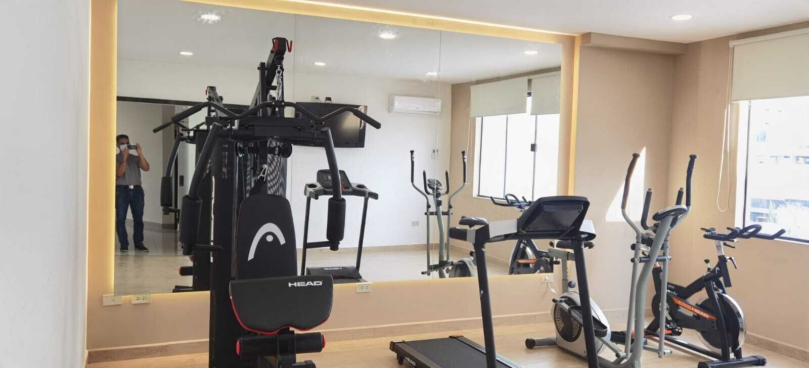 Un gimnasio con diversos equipos de ejercicio, incluyendo una cinta de correr, una elíptica y bicicletas estáticas.