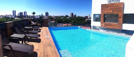 Ein Pool auf dem Dach mit Liegestühlen, Blick auf die Stadt und ein Gebäude mit der Aufschrift "Premium Suites".