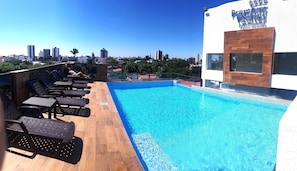 Una piscina en la azotea con sillones de descanso, vistas a la ciudad y un edificio con un letrero que dice "Premium Suites".