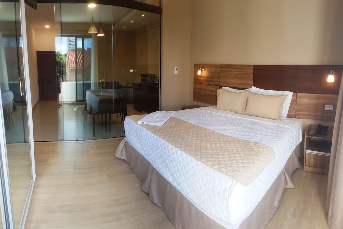Une chambre d’hôtel moderne avec un grand lit, une tête de lit en bois et une porte vitrée donnant sur un balcon.
