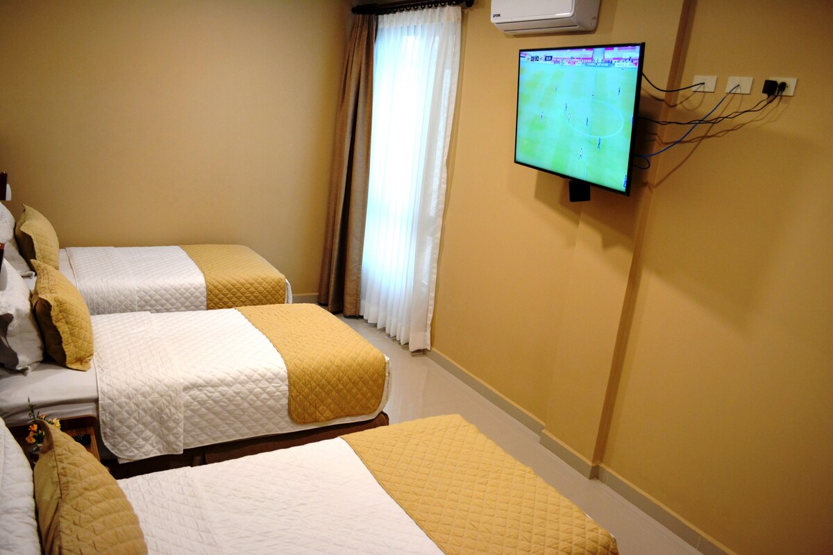 Ein Hotelzimmer mit zwei Betten, einem an der Wand befestigten Fernseher und einem Fenster mit Vorhängen.
