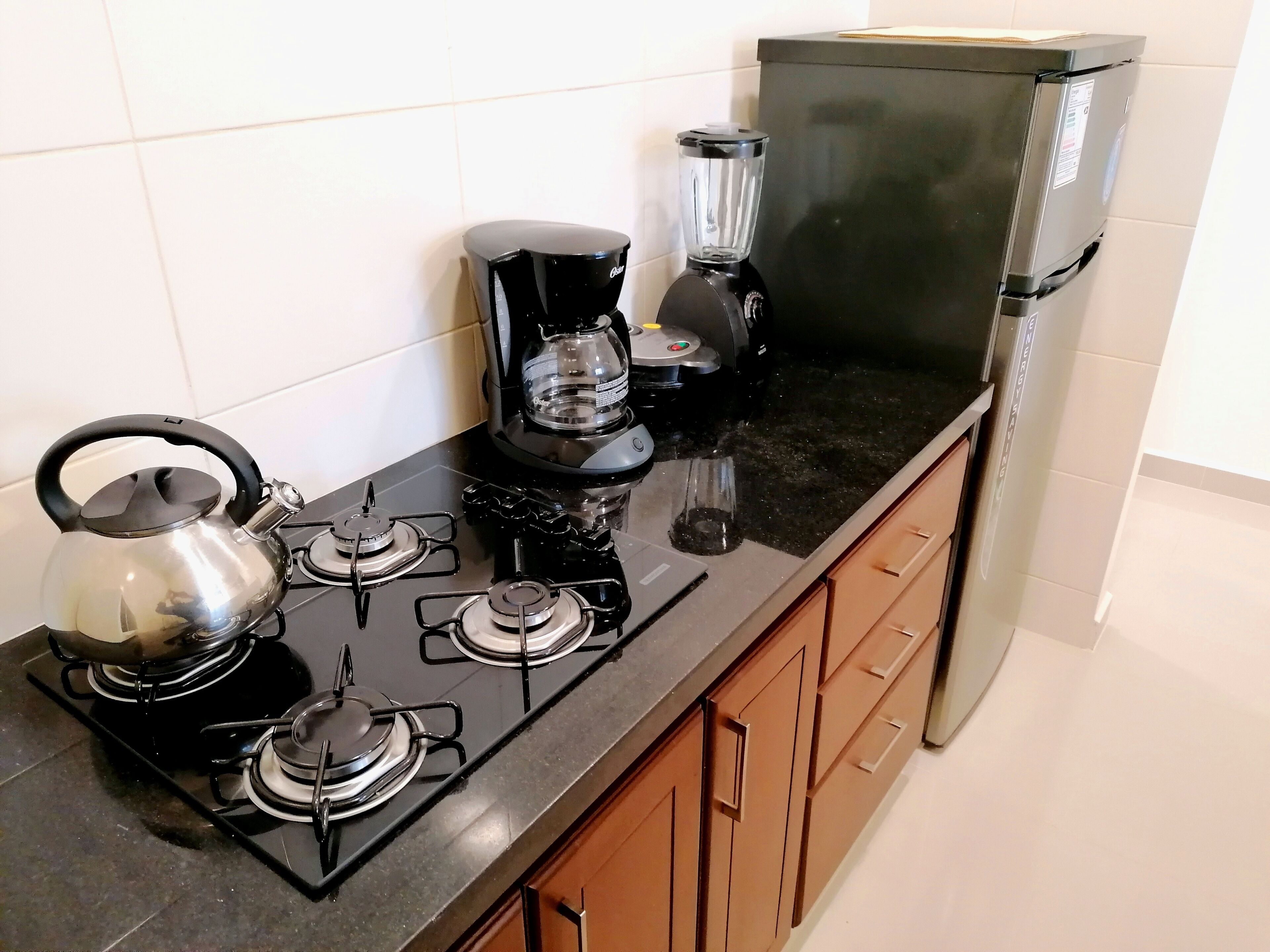 Una cocina equipada con estufa a gas, hervidor, cafetera, licuadora y refrigerador.