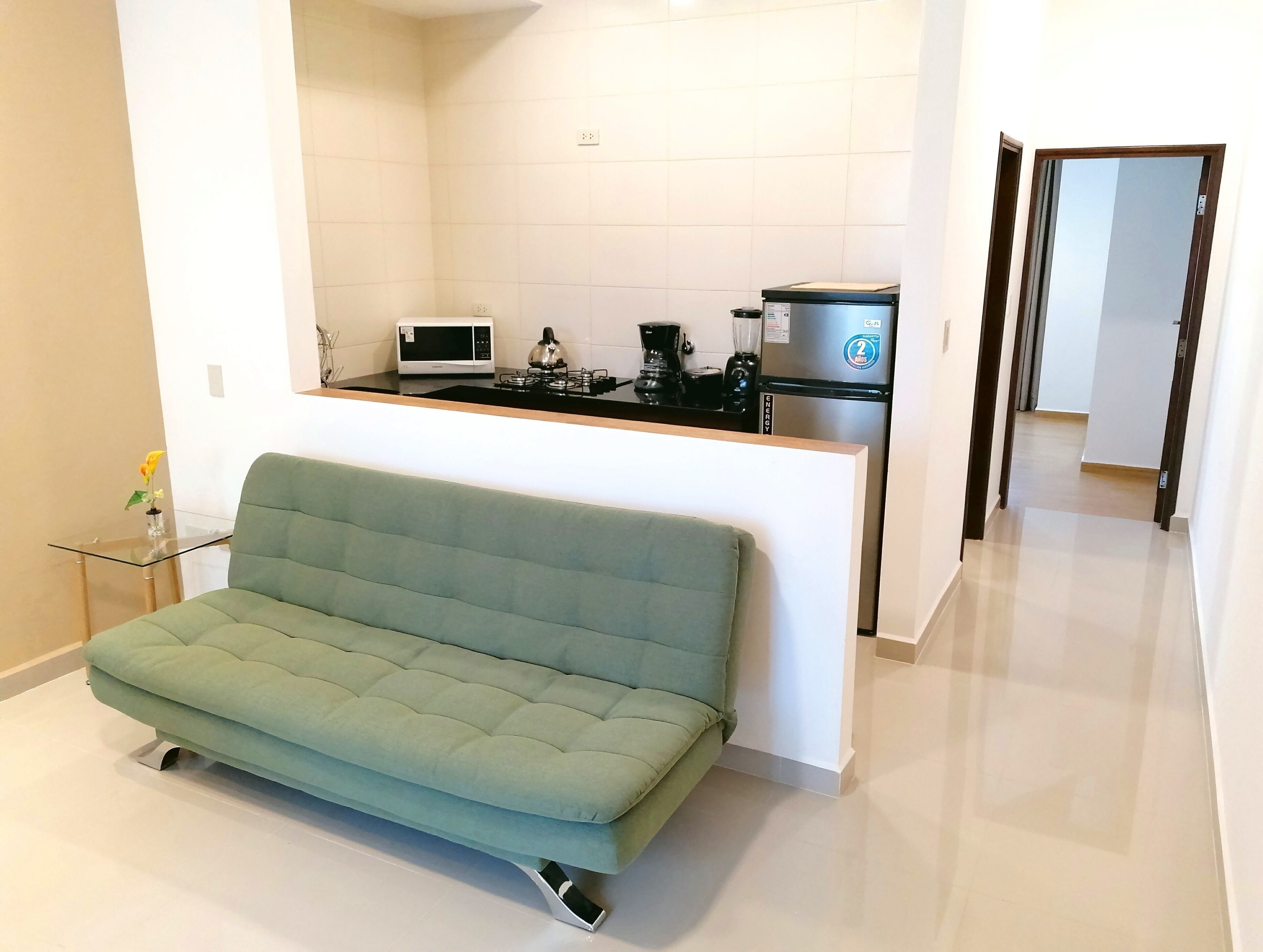 A modern kitchen with a built-in microwave, stove, and refrigerator. A green sofa is placed in front of the kitchen.