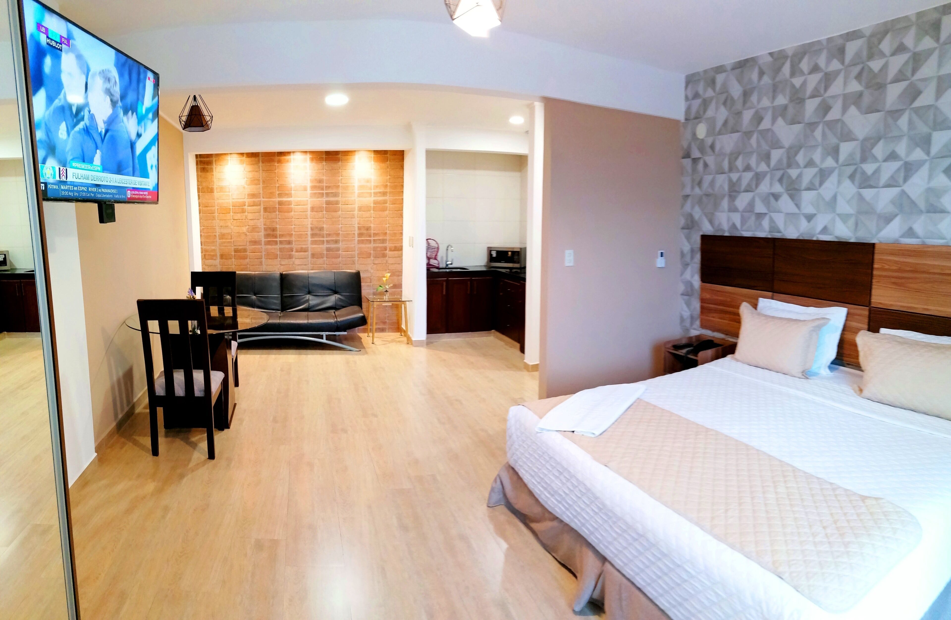 Een hotelkamer met een bed, een televisie, een zithoek en een keuken op de achtergrond.