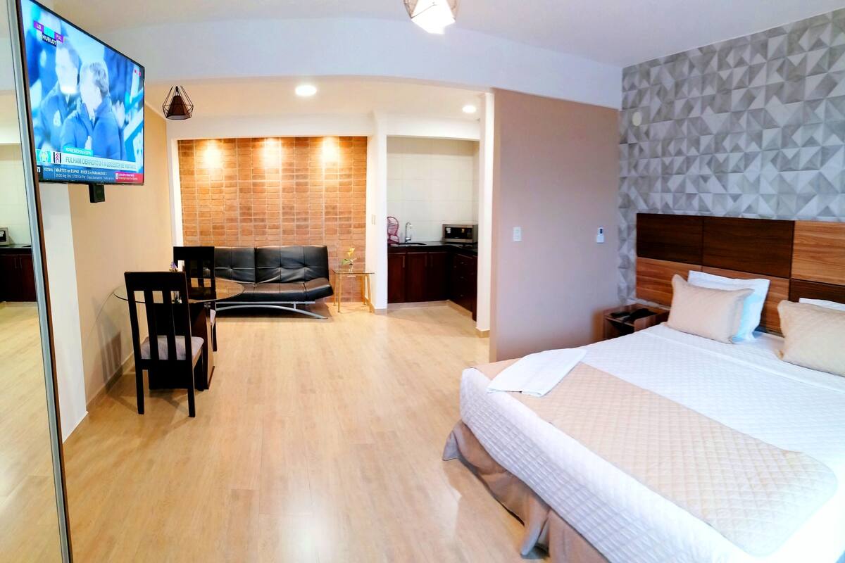 Une chambre d’hôtel avec un lit, une télévision, un coin salon et une cuisine à l’arrière-plan.