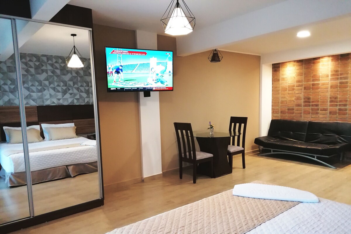 Ein Hotelzimmer mit Bett, Wandfernseher, einer Sitzecke mit Tisch und Stühlen sowie einem Sofa.