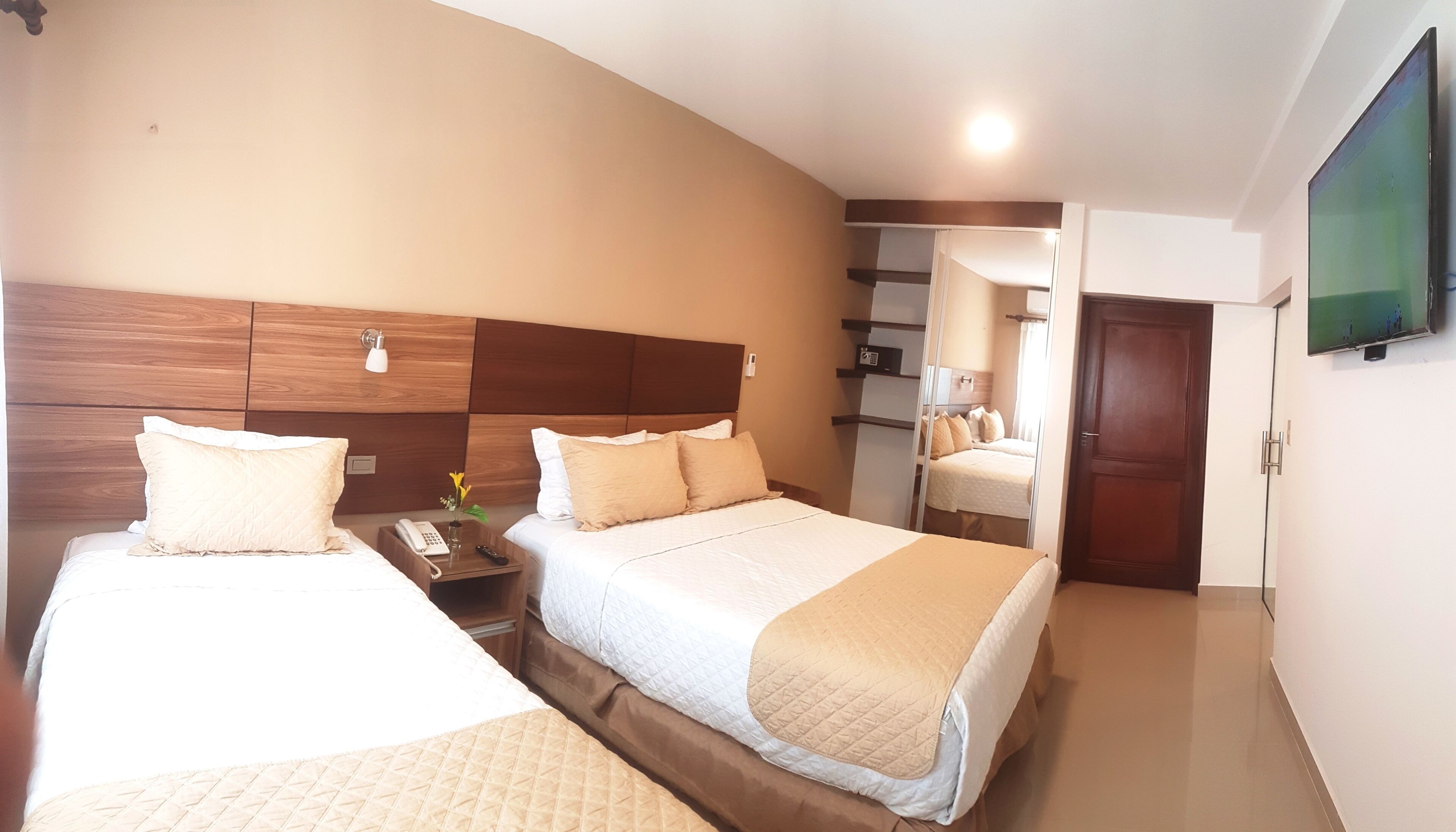 Een hotelkamer met twee bedden, een nachtkastje met een lamp, een televisie en een spiegel.