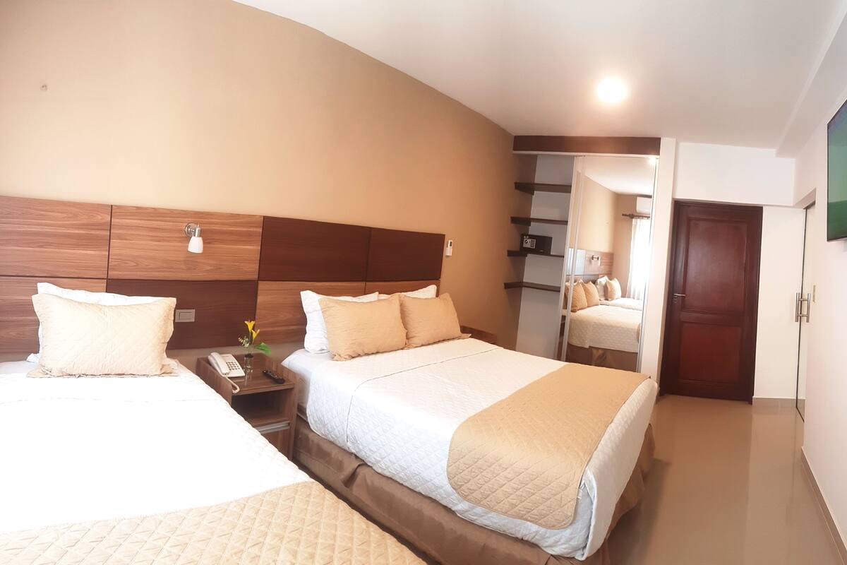 Une chambre d’hôtel avec deux lits, une table de chevet avec une lampe, une télévision et un miroir.
