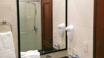 Un baño con un lavamanos negro, un espejo grande, una cabina de ducha de vidrio y un secador de pelo en la pared.