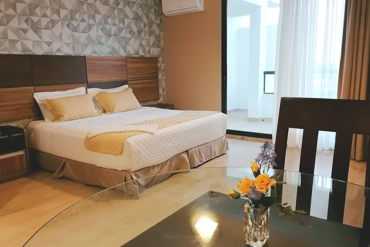 Une chambre d’hôtel avec un lit, une table de chevet et une table en verre ornée d’un vase de fleurs.