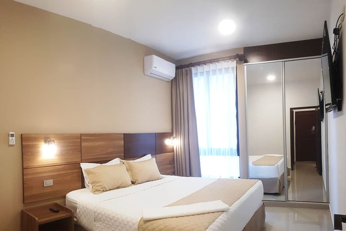 Une chambre d’hôtel moderne dotée d’un grand lit, de tables de chevet, d’un appareil de climatisation, d’un miroir et offrant une vue sur l’extérieur.